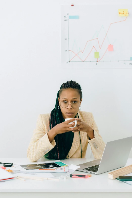 a woman sitting at a desk in front of a laptop, by Lily Delissa Joseph, next to a cup, data visualization, afro tech, serious business