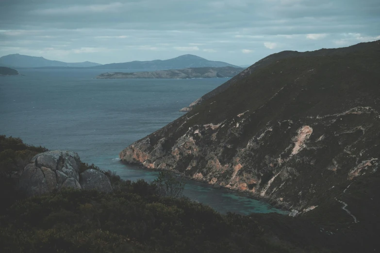 a large body of water sitting on top of a lush green hillside, a photo, unsplash contest winner, australian tonalism, croatian coastline, shades of blue and grey, in the distance is a rocky hill, lo fi