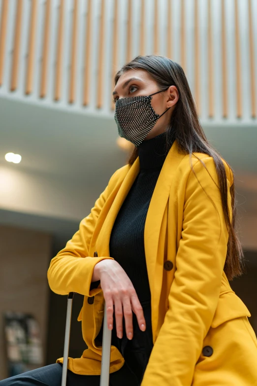 a woman with a face mask sitting on a suitcase, trending on pexels, renaissance, yellow clothes, wearing a blazer, in a mall, black facemask