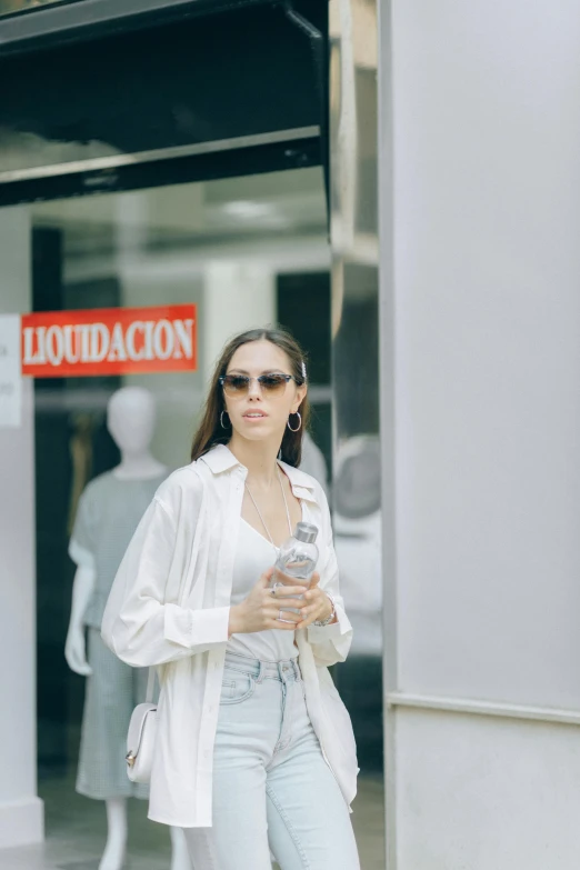 a woman standing in front of a store holding a cell phone, wearing white clothes, latinas, real trending on instagram image, candid photo of gal gadot