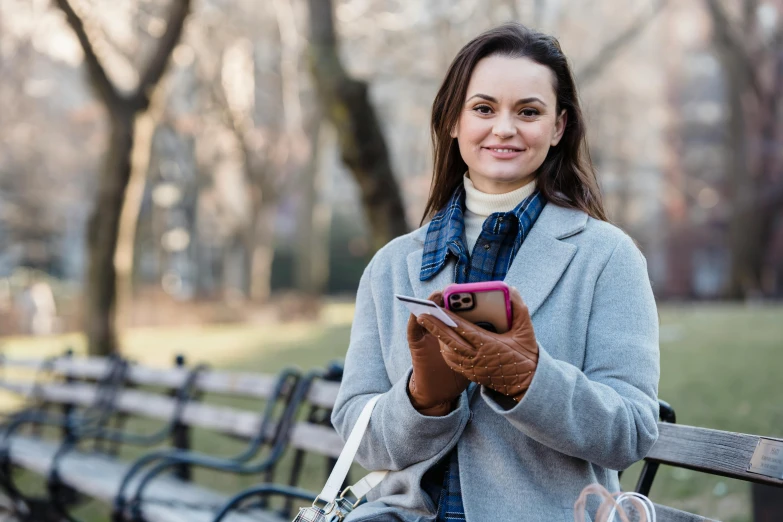 a woman sitting on a bench looking at her cell phone, a portrait, by Julia Pishtar, pexels contest winner, happening, central park, avatar image, holding a leather purse, mittens