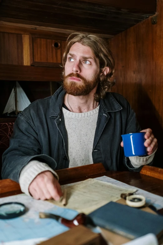 a man sitting at a table with a cup of coffee, trending on reddit, renaissance, rugged ship captain, hozier, wearing blue jacket, aboriginal australian hipster