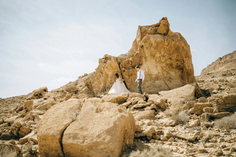 a man and a woman standing on top of a rocky hill, a photo, by Lee Loughridge, unsplash, romanticism, hillside desert pavilion, background image