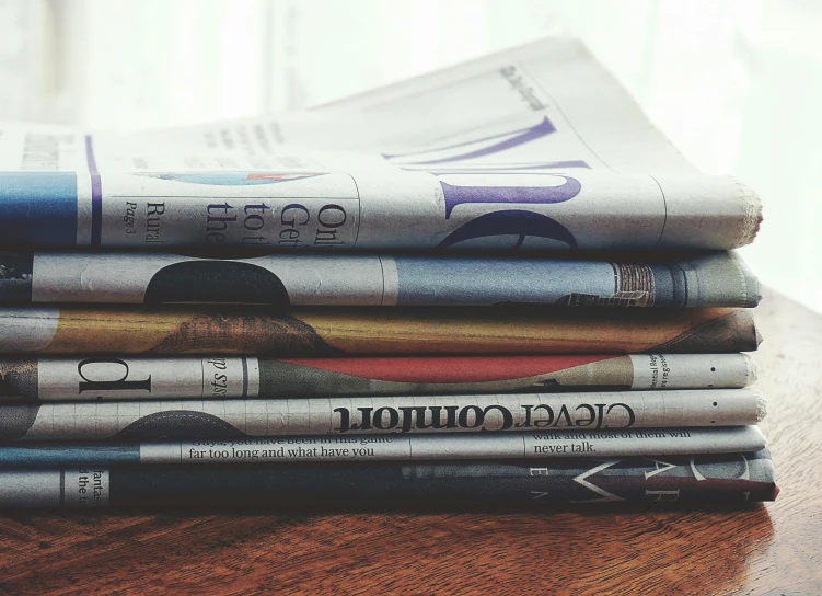 a stack of newspapers sitting on top of a wooden table, post appocalyptic, tubes, family friendly, split near the left