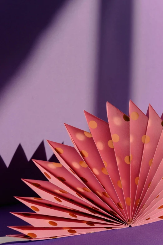 a close up of a folded paper flower on a table, by Julia Pishtar, trending on unsplash, conceptual art, crown of (pink lasers), fans, dots abstract, warm lighting with cool shadows