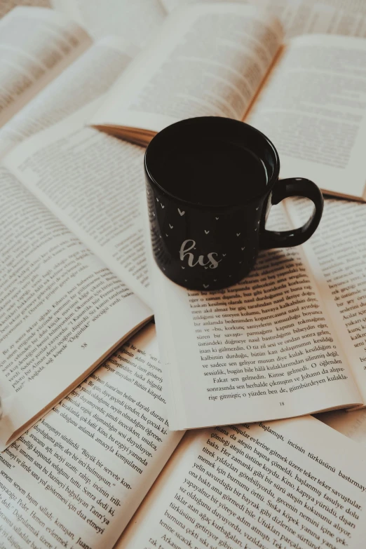 a cup of coffee sitting on top of an open book, black, promo image, multiple stories, unreadable text