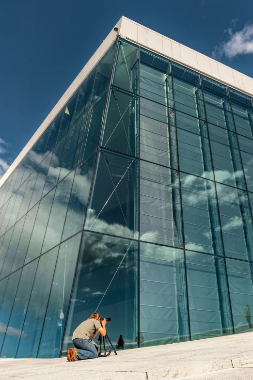 a man sitting on the steps in front of a building, inspired by Tadao Ando, unsplash, bauhaus, lots of glass details, clear blue skies, espoo, thumbnail