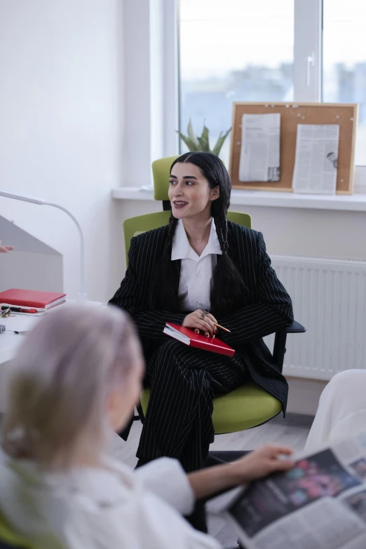 a woman sitting in a chair talking to another woman, lawyer clothing, a group of people, taken in 2 0 2 0, androgynous person