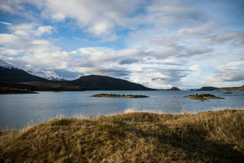 a body of water surrounded by grass and mountains, inspired by Þórarinn B. Þorláksson, unsplash, hurufiyya, patagonian, scattered islands, conde nast traveler photo, surrounding the city