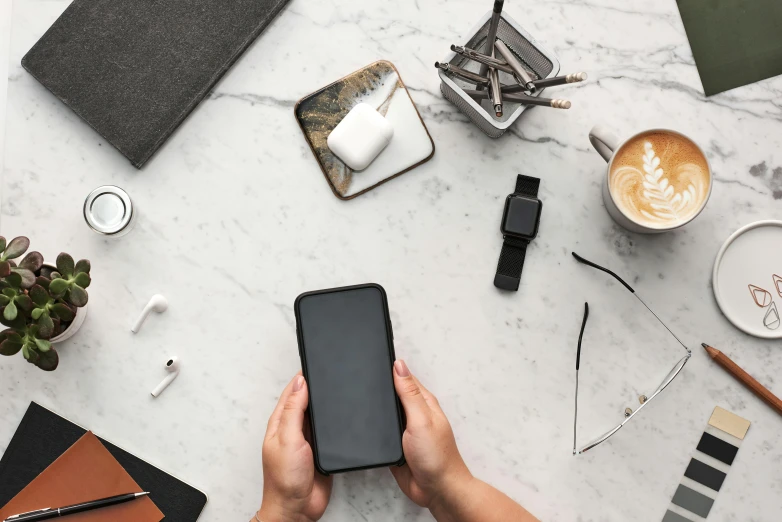 a person holding a smart phone on a table, 9 9 designs, white marble interior photograph, product shot, electronics