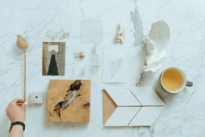 a person holding a piece of wood next to a cup of tea, a still life, inspired by Willem Claeszoon Heda, trending on unsplash, minimalism, white calacatta gold marble, an exquisite 3 d map, scattered rubbish and debris, various artworks