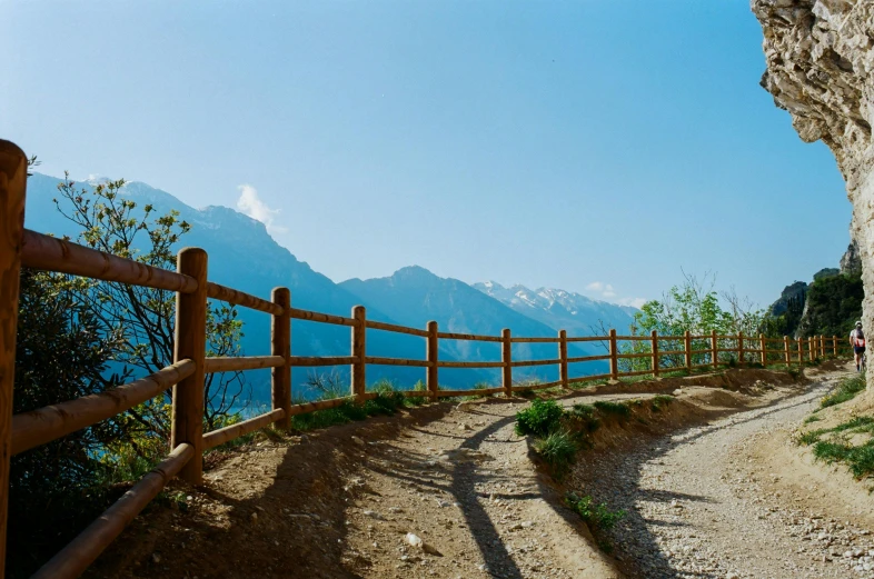a man riding a bike down a dirt road next to a wooden fence, by Matthias Weischer, unsplash, swiss alps, seaview, taken in the late 2000s, guardrail