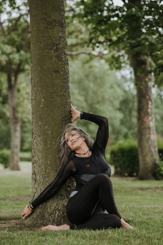 a woman leaning against a tree in a park, by Jan Tengnagel, unsplash, arabesque, wearing a black catsuit, yoga pose, cottagecore!! fitness body, grey