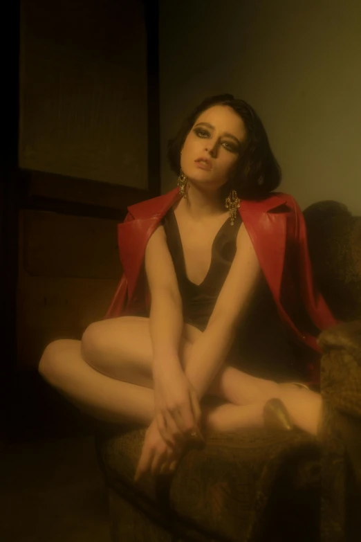 a woman sitting on a couch wearing a red cape, an album cover, inspired by George Hurrell, photorealism, joey king, phosphorescent, film noir style, she wears a jacket