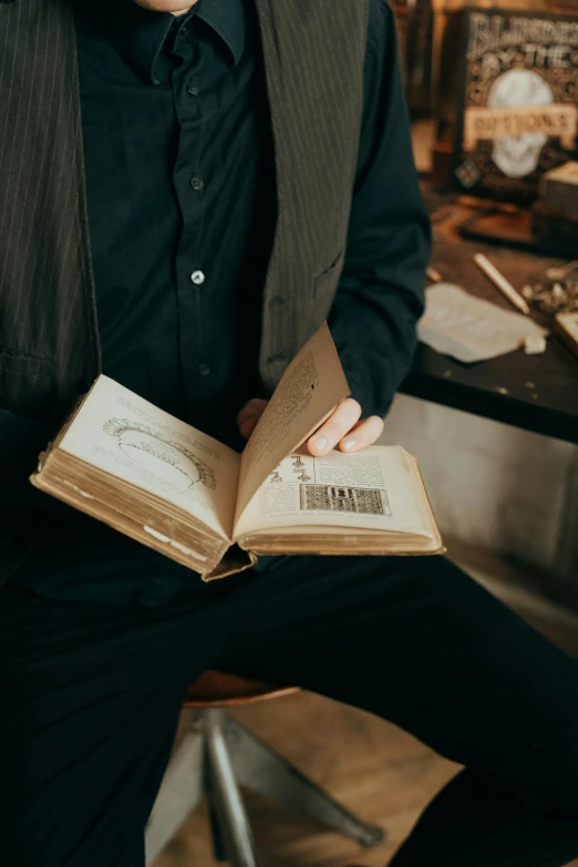 a man sitting on a chair holding a book, an album cover, by Jessie Algie, pexels contest winner, holding a pocket watch, inspect in inventory image, an open book, schematic in a notebook