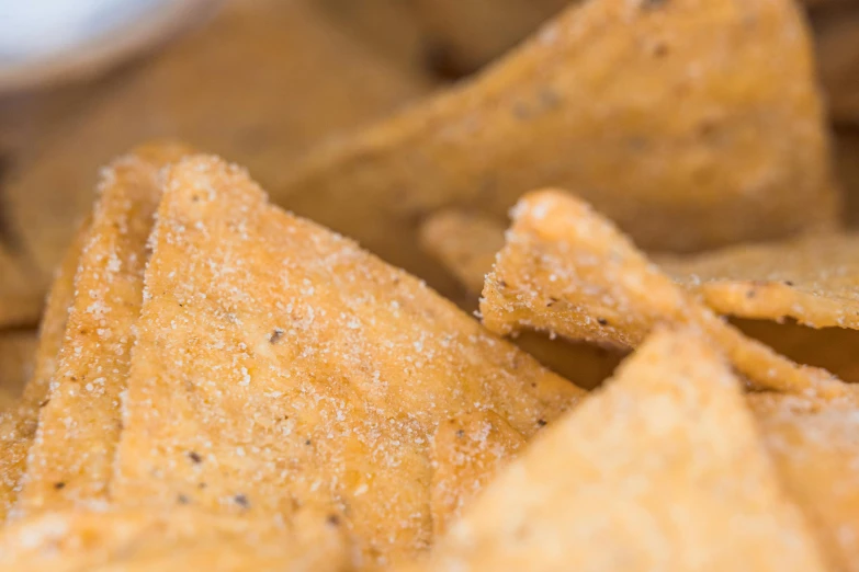 a pile of tortilla chips with a bowl of dip in the background, a macro photograph, by Carey Morris, pexels, visual art, squares, background image, dust, caramel