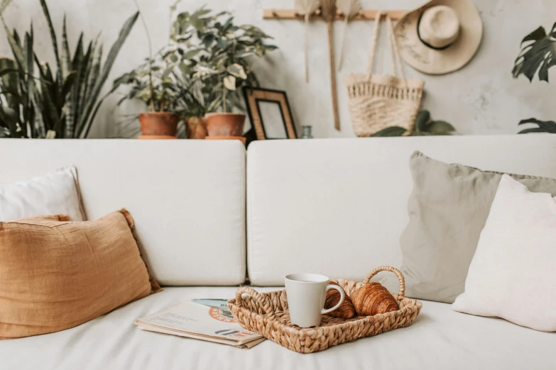 a basket filled with croissants sitting on top of a white couch, inspired by Constantin Hansen, pexels contest winner, boho neutral colors, with a white mug, interior of a small, botanicals