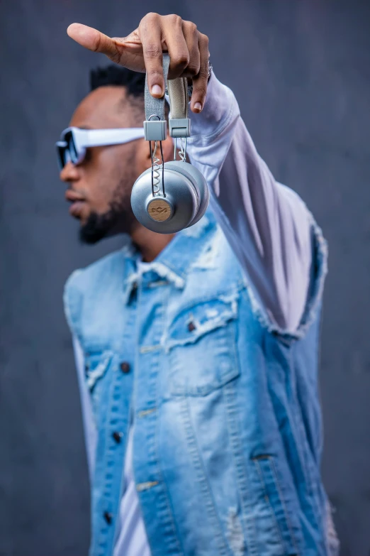 a man in a denim vest holding a pair of headphones, inspired by Ay-O, trending on pexels, hi mark ( akwaaba tommy ), press photos, lightening, stylish deity