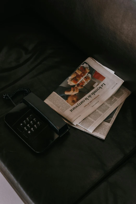 a cell phone sitting on top of a couch next to a newspaper, pexels contest winner, private press, matte black paper, toaster, black beret, telephone