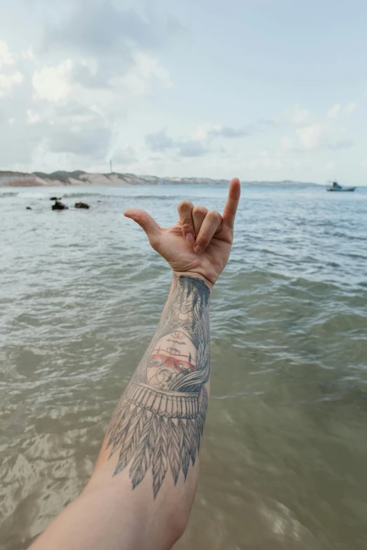 a person standing in the water with a tattoo on their arm, pexels contest winner, viewed from the ocean, middle finger, photograph of a sleeve tattoo, manly