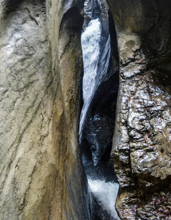 a man standing on top of a rock next to a waterfall, inside the tunnel, photo taken from above, hanging veins, thumbnail