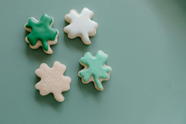 four decorated cookies sitting on top of a green table, trending on pexels, four leaf clover, background image, minimalistic aesthetics, on a pale background