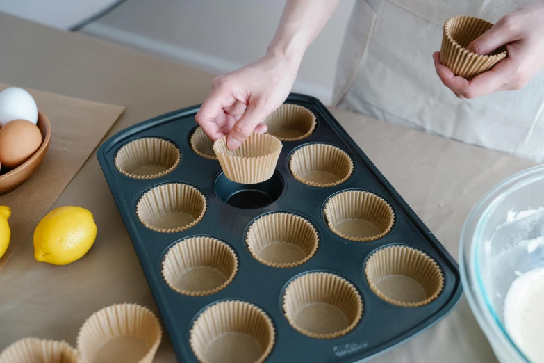 a person placing a cupcake in a muffin tin, by Helen Stevenson, lemon, professionally assembled, brown, medium range