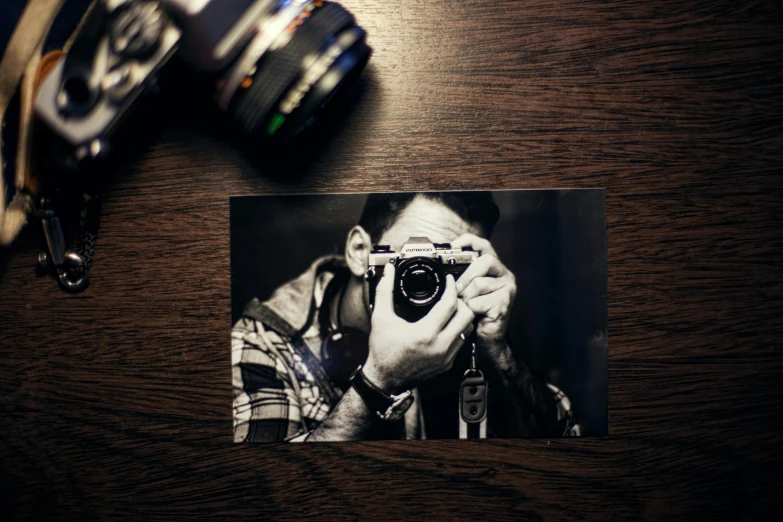 a black and white photo of a man holding a camera, a black and white photo, pexels contest winner, on a wooden table, colored photo, low-light photograph, camera looking down upon
