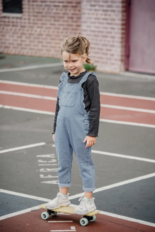 a little girl standing on top of a skateboard, inspired by Myles Birket Foster, unsplash, wearing prison jumpsuit, slate, wearing overalls, with two front pockets