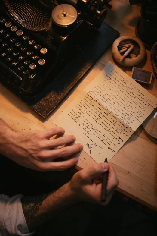a person writing on a piece of paper next to a typewriter, an album cover, unsplash, autochrome, ignant, high angle shot, a wooden