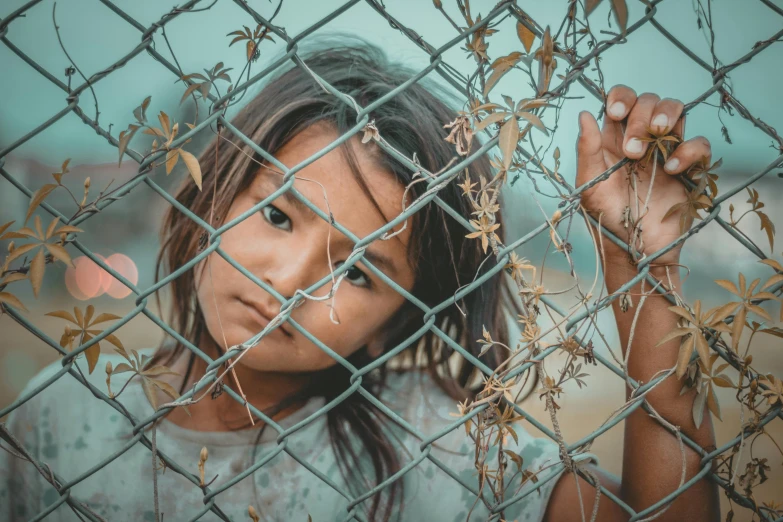 a young girl standing behind a chain link fence, pexels contest winner, migrant mother, square, indian girl with brown skin, stylized