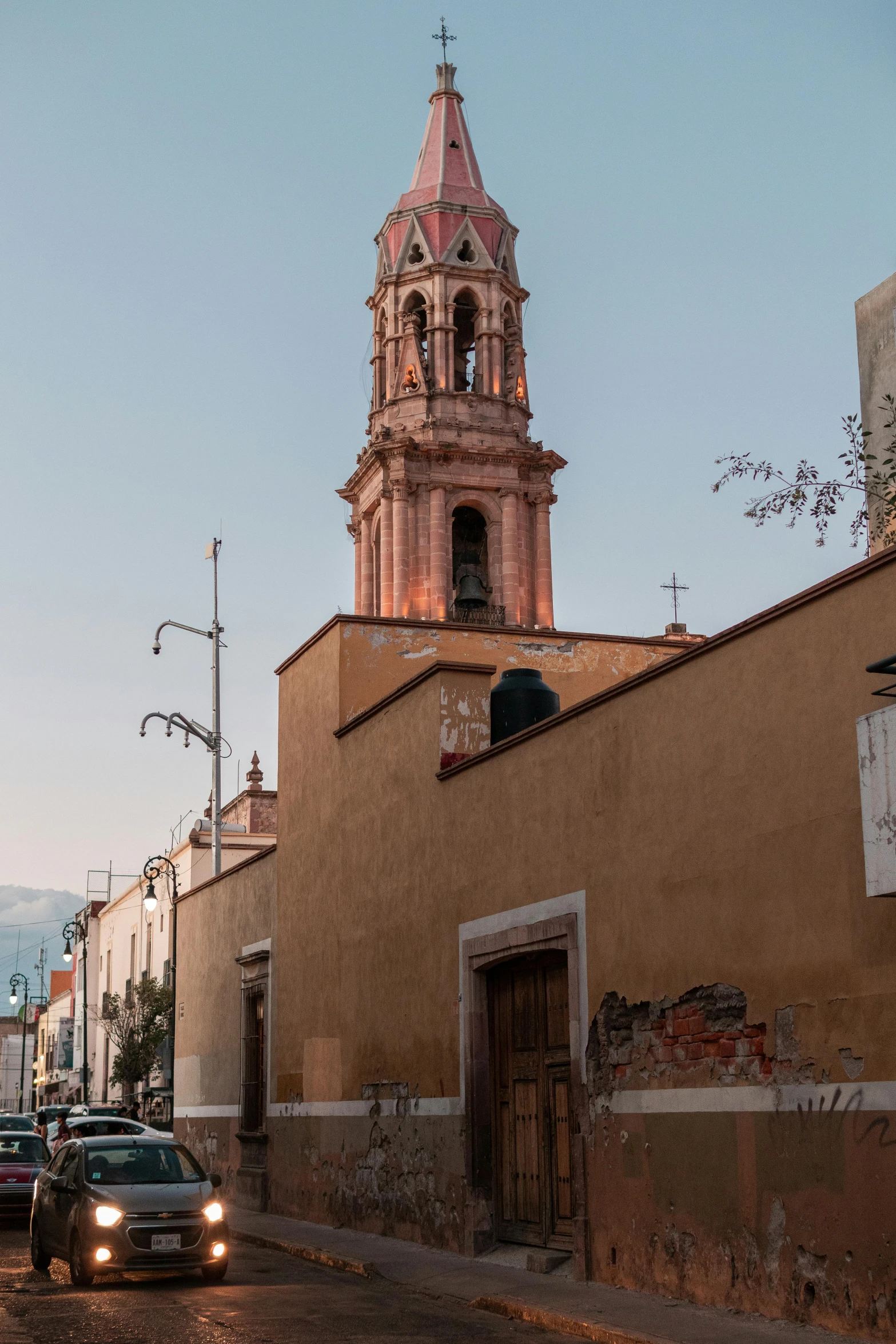 a car driving down a street next to a tall building, inspired by Joaquín Torres García, neoclassical tower with dome, tlaquepaque, pink golden hour, churches