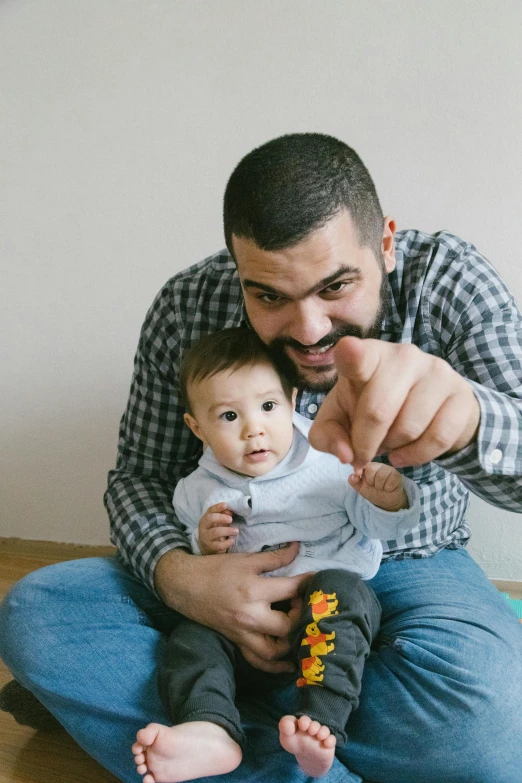 a man sitting on the floor holding a baby, a cartoon, pexels contest winner, dada, pointing index finger, unibrow, romanian, gif