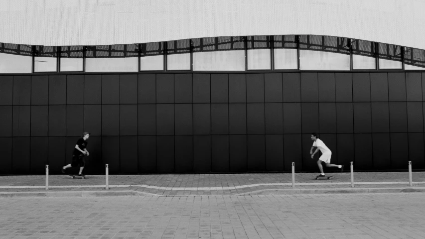 a couple of men riding skateboards down a sidewalk, a black and white photo, pexels contest winner, postminimalism, athletic crossfit build, in empty!!!! legnica, behind the wall, sprinting