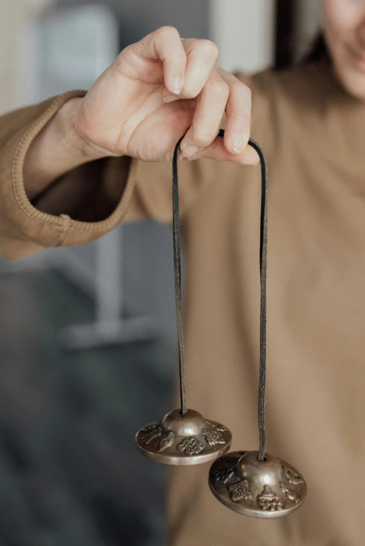 a close up of a person holding two bells, inspired by Gong Kai, kinetic art, metal handles, vanilla, worn, incense