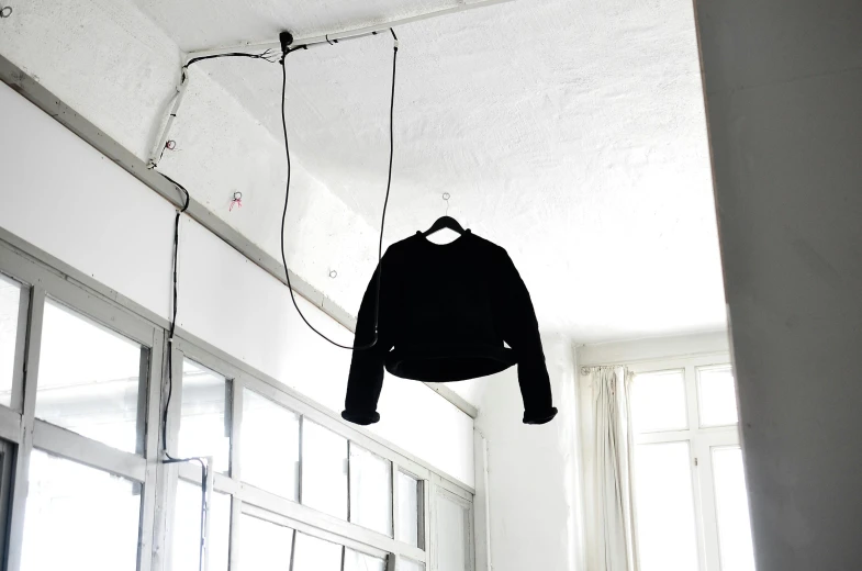 a black sweater hanging from a ceiling in a room, by Nina Hamnett, neo-dada, wire management, raphael personnaz, electric arc, ( ( dieter rams ) )