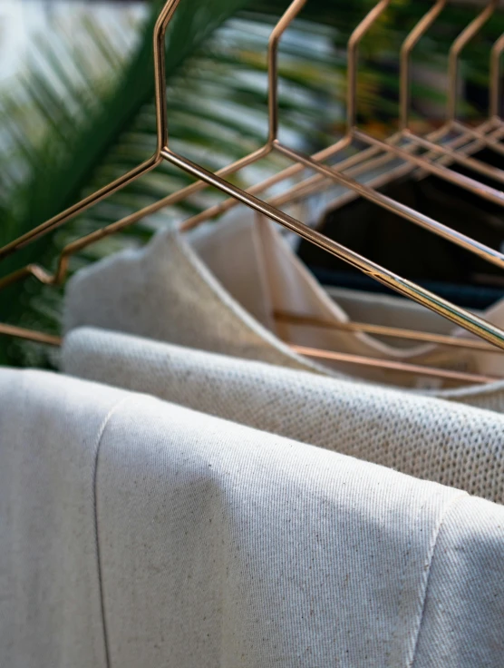 a bunch of clothes hanging on a clothes rack, by Alice Mason, material brass & copper gold, close - up on detailed, soft filtered outdoor lighting, light beige pillows