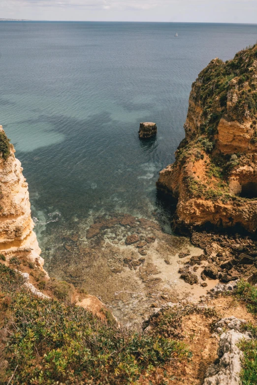 a person standing on top of a cliff next to the ocean, rocha, deep clear pools of water, rock arches, looking down from above