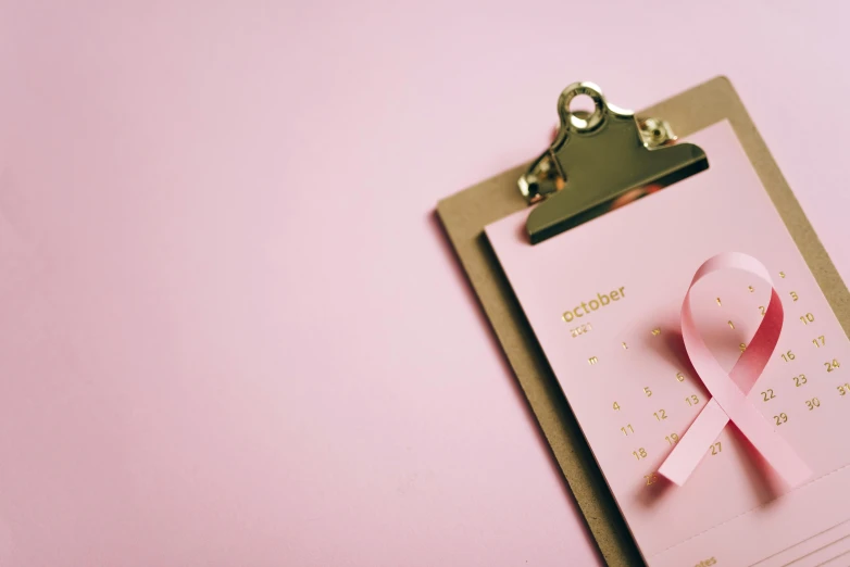 a clipboard with a pink ribbon on it, by Julia Pishtar, pexels contest winner, female calendar, golden ribbon, background image, pink skin