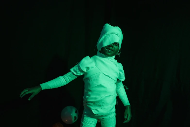 a little boy dressed up as a mummy, by Elsa Bleda, pexels contest winner, happening, green neon, wearing white cloths, in a pitch black room, alexis franklin