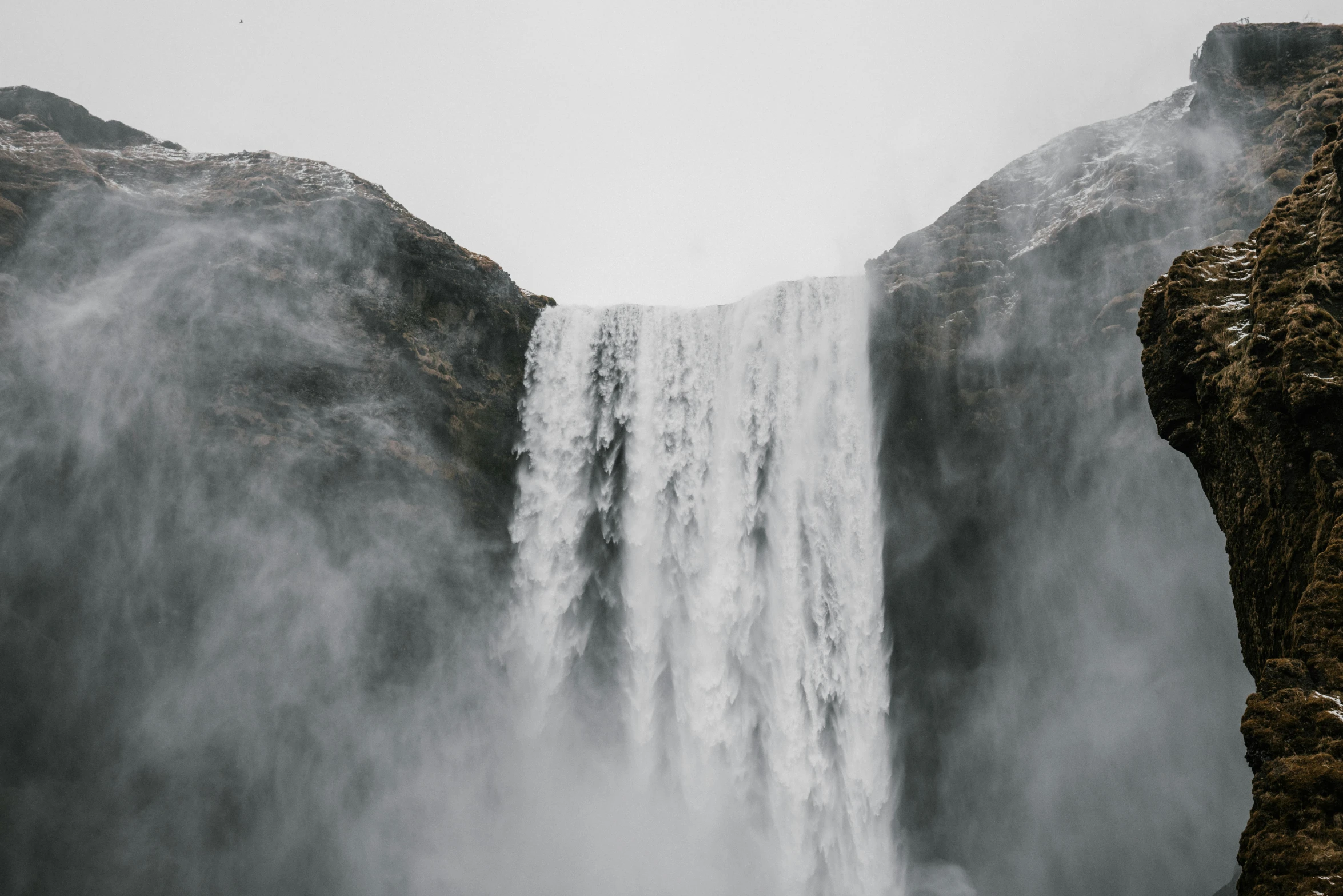 a man standing on top of a cliff next to a waterfall, pexels contest winner, romanticism, grey mist, background image, shot from below, white fog painting