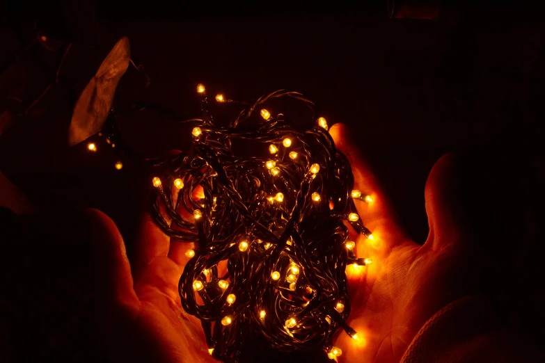 a person holding a string of lights in their hands, an album cover, inspired by Elsa Bleda, reddit, coloured in orange fire, taken with sony alpha 9, christmas night, yellow