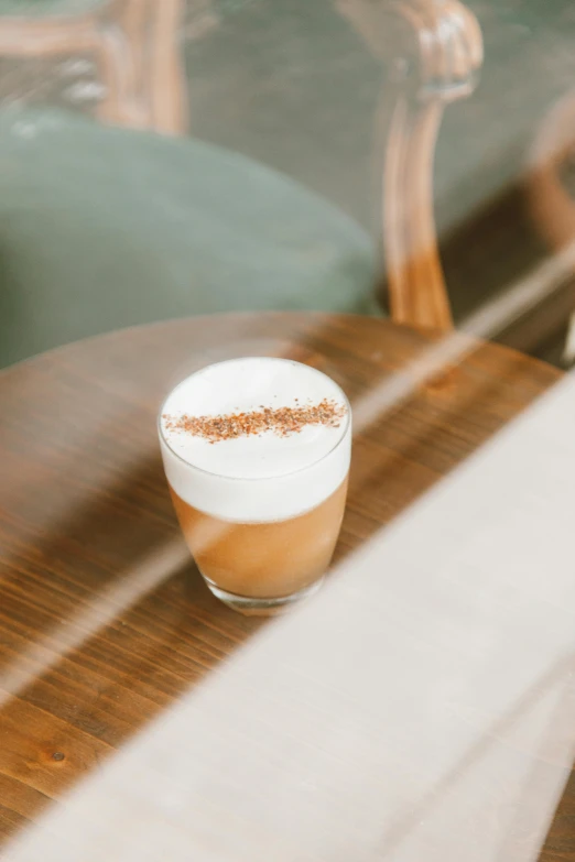 a cup of coffee sitting on top of a wooden table, cocktail in an engraved glass, thumbnail, subtle detailing, whipped cream on top