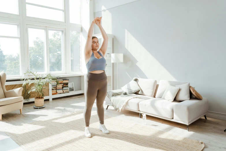 a woman standing in a living room with her arms in the air, pixeled stretching, promo image, overweight, background image