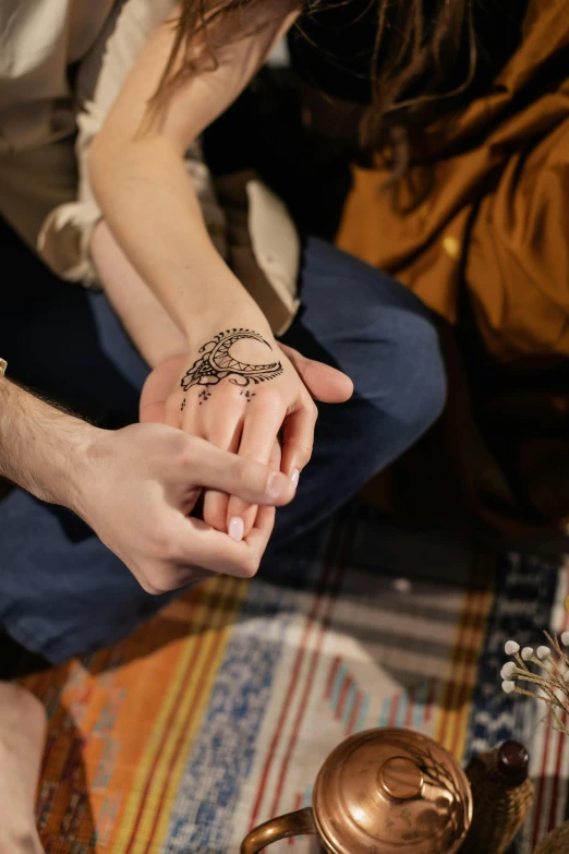 a woman sitting on a rug with a tattoo on her arm, trending on pexels, hurufiyya, couple walking hand in hand, arabian night, hands shielding face, indoor setting