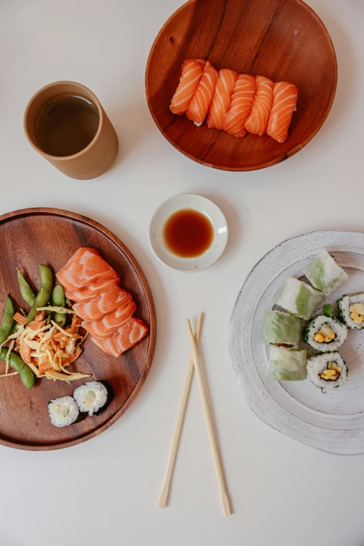 a table topped with plates of sushi and chopsticks, flatlay, medium angle, salmon, clean lines