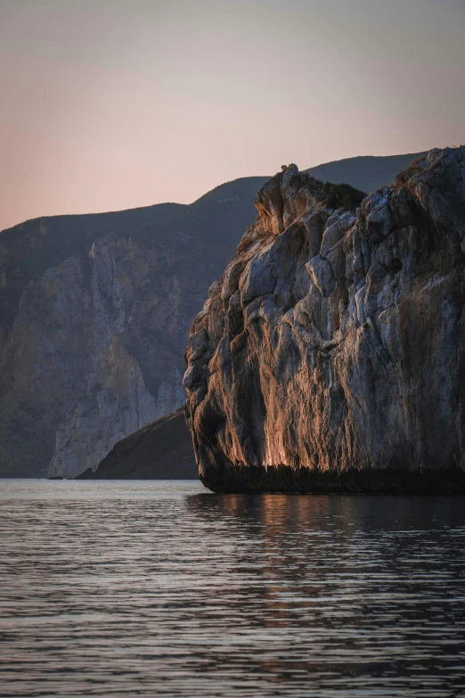 a large rock in the middle of a body of water, cliff side at dusk, byzantine, fjords, lush surroundings