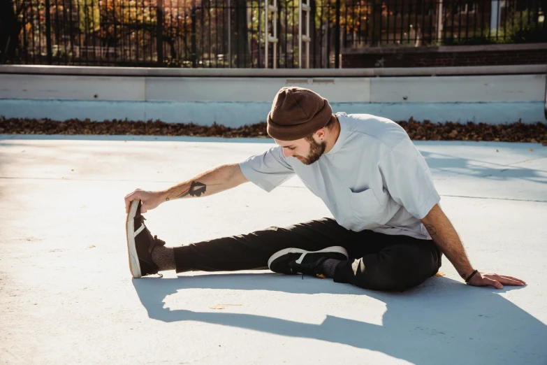 a man sitting on the ground with a skateboard, stretch, lynn skordal, warm, outside on the ground