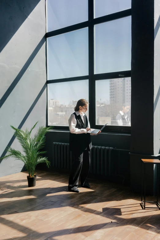 a woman standing in front of a window with a laptop, neo kyiv, floor - to - ceiling windows, black windows, carrying a tray