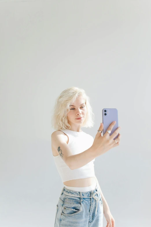 a woman taking a selfie with her cell phone, inspired by Elsa Bleda, minimalism, pale hair, bare midriff, all white, non-binary